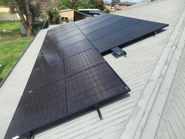 Panneaux solaires noirs Photon Solaris sur toit en tôle inclinée à Fleurance, maisons et jardins en arrière-plan